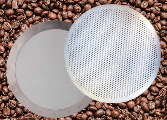 Two stainless steel Aeropress reusable filters, the disk and mesh type, with coffee beans in the background