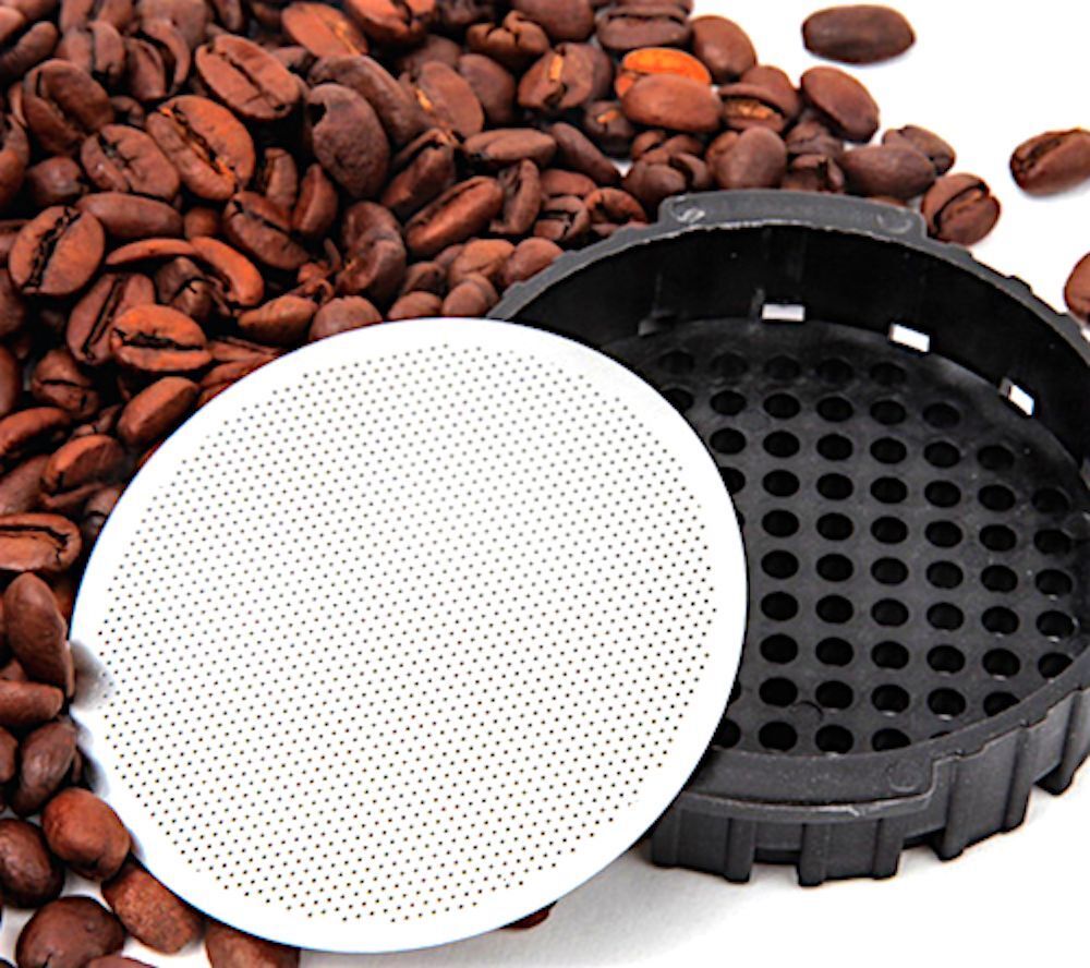 Stainless steel disk AeroPress coffee filter leaning against filter basket with pile of coffee beans – reusable, eco-friendly